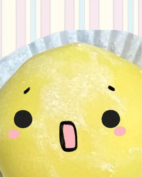 A yellow mango mochi in its paper cup, dusted with starch, with a surprised face drawn on