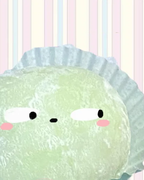 A pale green matcha mochi in its paper cup, dusted with starch, with a sleepy face drawn on